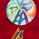 rainbow windmill with colored pencils below it on red backdrop